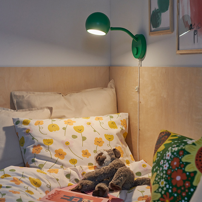 Un dormitorio que cuenta con una lámpara KORVSNÖRE verde y un juego de funda nórdica BARNDRÖM con estampado floral, dispuesto sobre una cama.