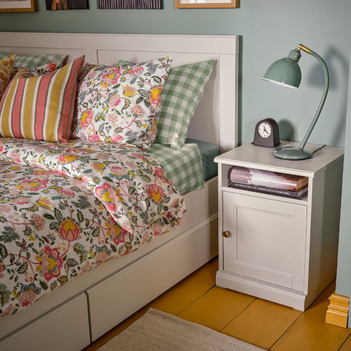 A bedroom with a FÅGELFJÄLLET bedside table and bed dressed in floral DAGGSALVIA bedding.