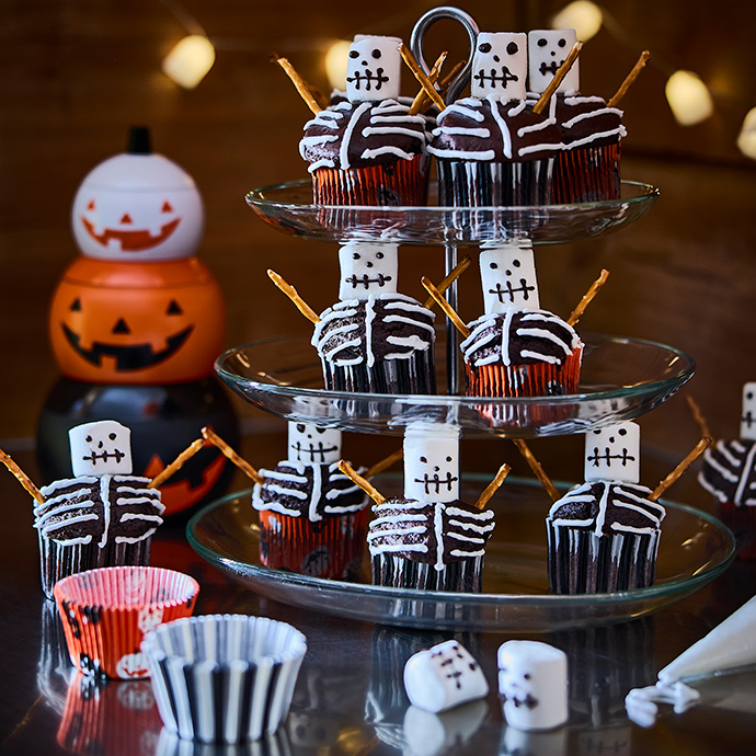 Un soporte para pasteles de tres niveles lleno de cupcakes caseros con temática de esqueletos, colocados en moldes para hornear KUSTFYR.