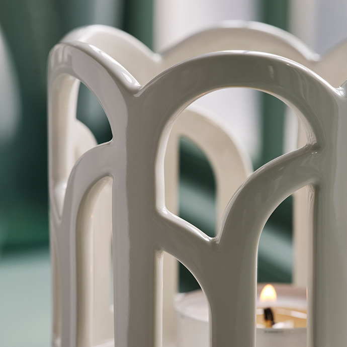 A close-up of a SNÖSISKA candle holder in off-white. The pigmented glaze on the stoneware shines when it catches the light.