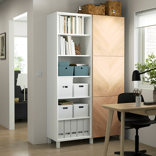 Mueble columna BESTÅ blanco con compartimentos abiertos/cerrados, con capacidad para libros y decoración, rodeado de muebles de madera en una habitación luminosa.