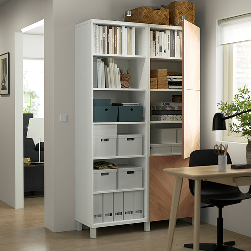 Una moderna oficina en casa, una estantería BESTÅ con estantes ajustables que contienen libros y cajas de almacenamiento, junto a un escritorio con una silla y plantas.