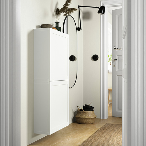 Moderno armario blanco BESTÅ, más alto que una cesta, con elegantes asas negras y lámpara, cerca de la puerta.