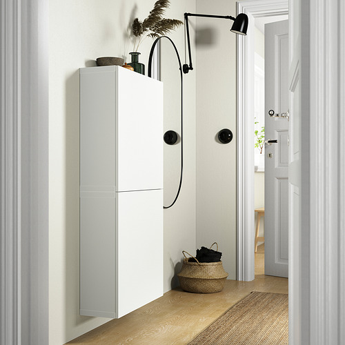 Moderno armario de pared blanco BESTÅ con elegantes pomos negros; Alto, estrecho, cabe en el pasillo junto a la cesta de mimbre y la lámpara.