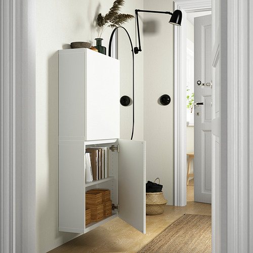 Un pasillo moderno, un armario de pared blanco BESTÅ con estantes ajustables, libros y una cesta de mimbre. Una luz montada en la pared añade funcionalidad.