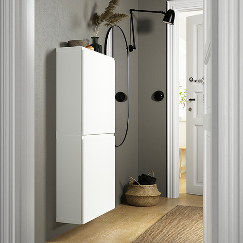 Pasillo moderno con armario de pared BESTÅ en blanco, más alto que la cesta de la puerta, junto a la lámpara de pared.