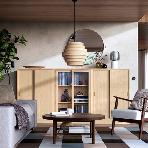 Moderno salón con mueble de madera clara TONSTAD, espejo redondo, lámpara colgante única, sofá gris, mesa de centro, alfombra de rayas y sillón.