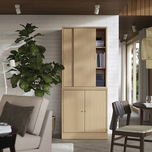 Sala de estar minimalista con mueble de madera clara, sillas, planta y luz natural.