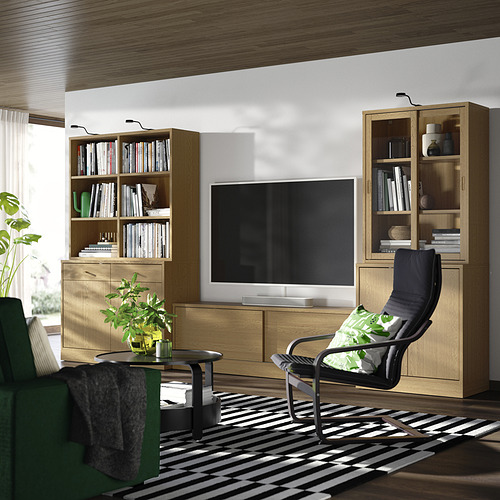 Sala de estar moderna: televisor negro, estantes de madera, mecedora negra, planta, alfombra blanca y negra, iluminación tenue.