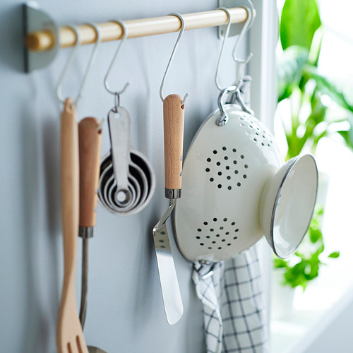 Los utensilios de cocina cuelgan cuidadosamente de los ganchos de la pared. Incluye cuchara ranurada, espátulas y tazas medidoras. La espátula tiene mango de madera y orificio para colgar.