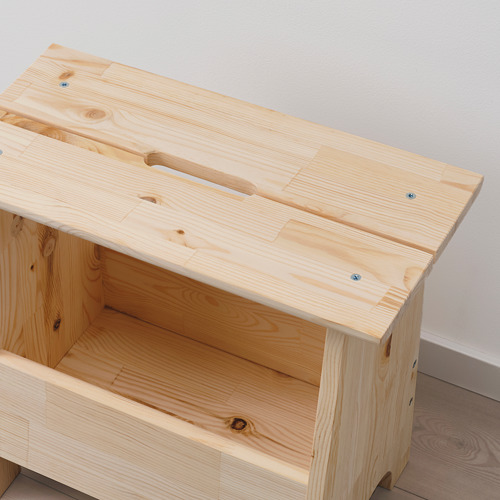 Taburete simple de madera con almacenamiento abierto debajo. Madera de pino claro, acabado natural. Recorte del asa en la parte superior para facilitar el movimiento.