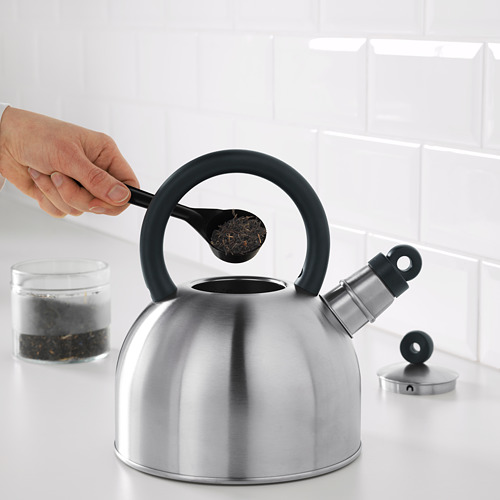 La mano vierte hojas de té en una tetera VATTENTÄT silbante en la estufa.