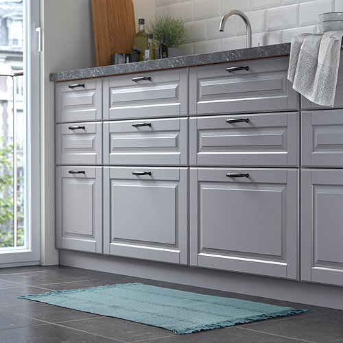 Cocina con armarios grises, fregadero y una alfombra rectangular azul en el suelo.
