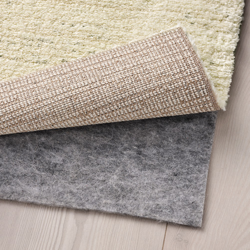 Una alfombra beige texturizada sobre suelos de madera con una alfombrilla antideslizante debajo, que muestra su durabilidad y seguridad.