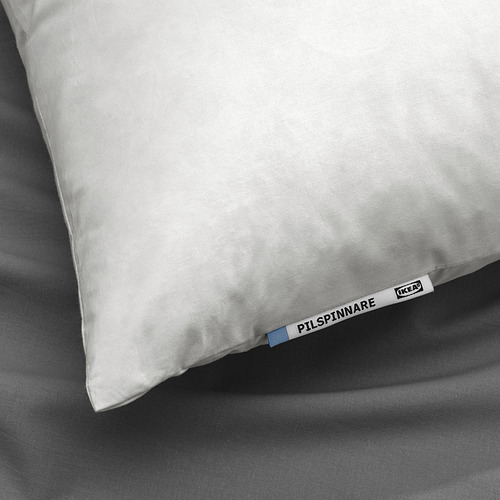 Un primer plano de una almohada blanca sobre una cama gris, etiquetada como PILSPINNARE con la marca ikea, que enfatiza la comodidad y la calidad.