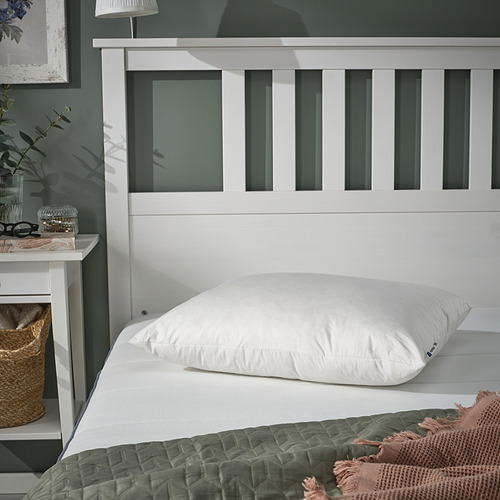Almohada rectangular blanca sobre la cama, rellena de plumas, cerca de la lámpara.