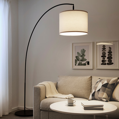 Salón moderno con lámpara RINGSTA, gran pantalla blanca, soporte negro. Sofá beige, almohadas estampadas, mesa de centro, obras de arte.