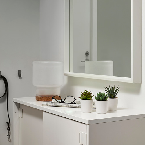 Moderna encimera de baño con mueble blanco, espejo, plantas artificiales FEJKA y lámpara. Gancho para lavandería y libro también.
