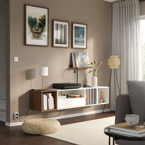Modern living room with EKET shelf, record player, books, lamp, and art. Grey couch, standing lamp, and sheers by window.