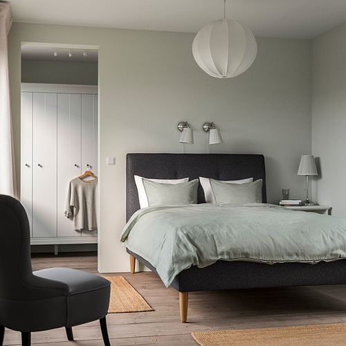 Dormitorio moderno con cama IDANÄS, lámpara colgante, silla negra, armario blanco y alfombras ligeras.