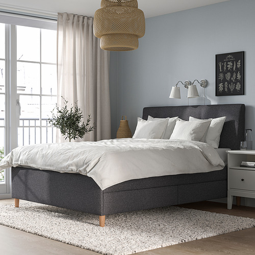 Dormitorio moderno con cama IDANÄS gris oscuro, almohadas blancas, planta y alfombra. Ambiente relajante.