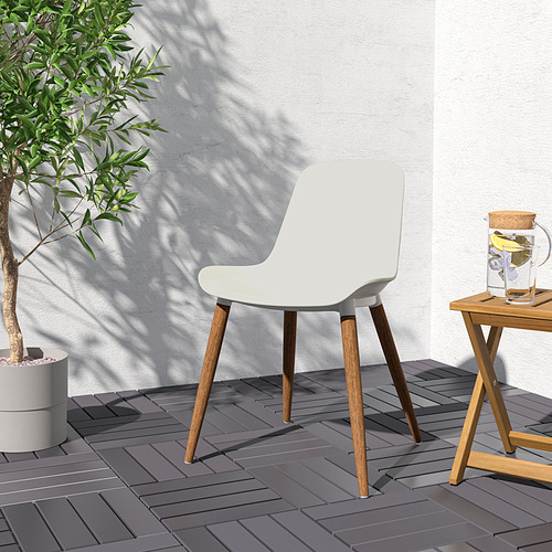 Silla GRÖNSTA blanca con patas de madera, diseñada para mayor comodidad y fácil limpieza, colocada al aire libre cerca de una mesa con una jarra de agua y una planta en maceta.