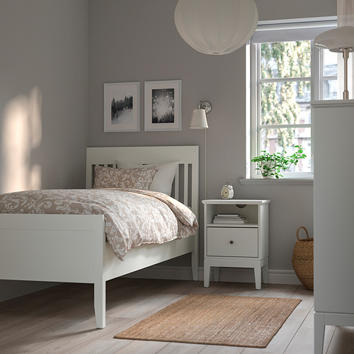 Dormitorio con cama blanca, mesita de noche gris, alfombra tejida y lámpara colgante ÅRSTID.