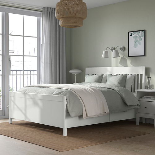 Cama IDANÄS blanca moderna con cajones de almacenamiento, diseño elegante, pared verde claro, mesitas de noche, ropa de cama suave, ventana grande, ambiente acogedor.