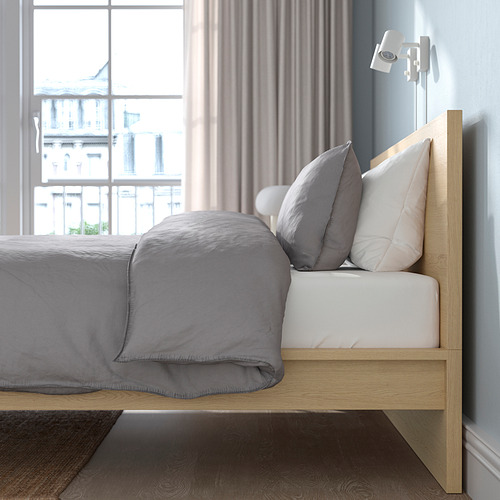 Cama minimalista con cabecero de madera, ropa de cama gris, por gran ventanal con laterales ajustables y somier.
