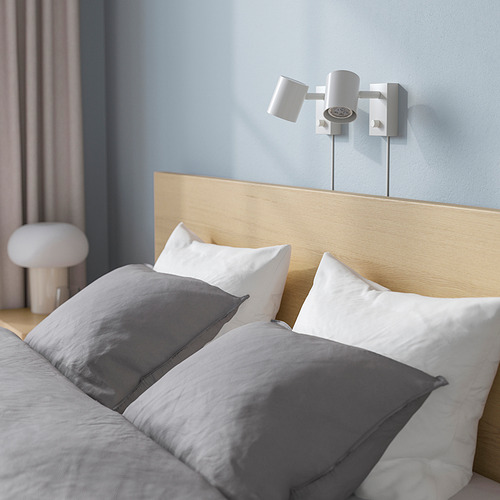 Cama moderna con cabecero de madera, apliques y ropa de cama gris. La cabecera proporciona soporte para la espalda para leer o ver la televisión.