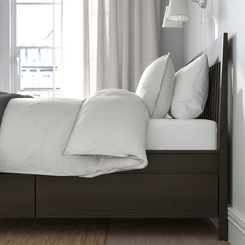 Cama moderna con diseño minimalista, cuatro cajones de cierre suave debajo, tela de color claro y marco de cama de madera oscura.