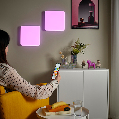 Una mujer usa un teléfono inteligente para ajustar los paneles de luz inteligentes, cambiando el estado de ánimo de las habitaciones con una iluminación colorida.