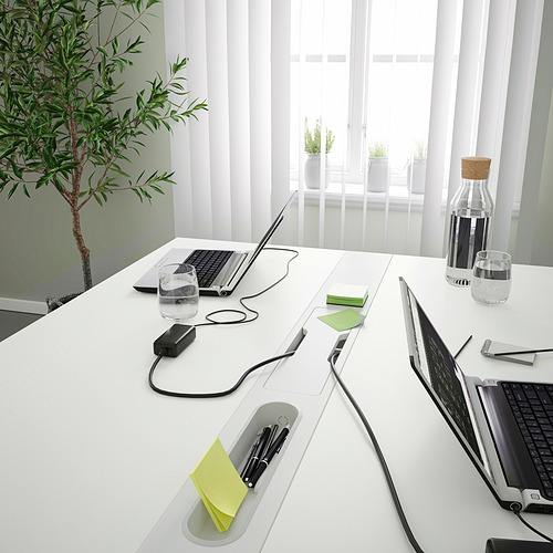 Una moderna mesa de conferencias con conexiones integradas para portátiles y gestión de cables. La superficie de la mesa tiene blocs de notas, una botella de agua y vasos.