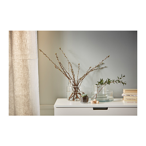 Una estantería blanca con jarrones decorativos de cristal de diferentes tamaños que contienen ramas y pequeñas plantas dispuestas ordenadamente.