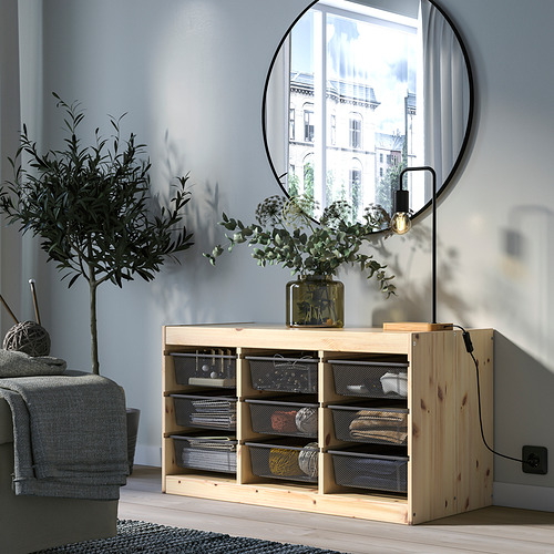 Afirmado, mueble de almacenaje de madera clara TROFAST, cajas de malla gris, espejo de pared redondo, planta verde, sofá gris, suelo de madera, pared gris claro.