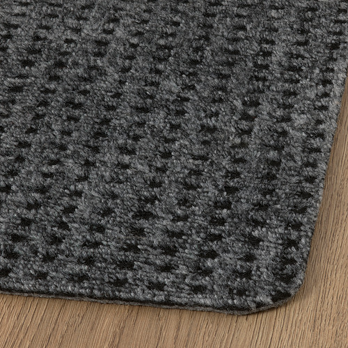 Felpudo gris con superficie texturizada, colocado sobre suelo de madera, que muestra su diseño duradero y elegante.