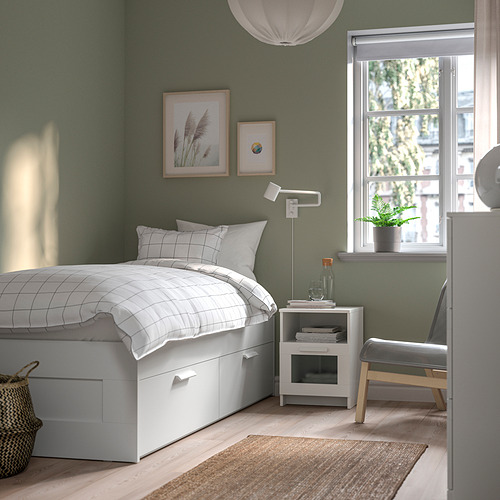 Dormitorio pequeño y moderno con cama blanca BRIMNES contra la pared verde. Silla blanca minimalista, mesita de noche, planta y obras de arte.