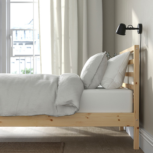 Dormitorio escandinavo con cama TARVA, ropa de cama blanca, lámpara de pared y vista a la ciudad.