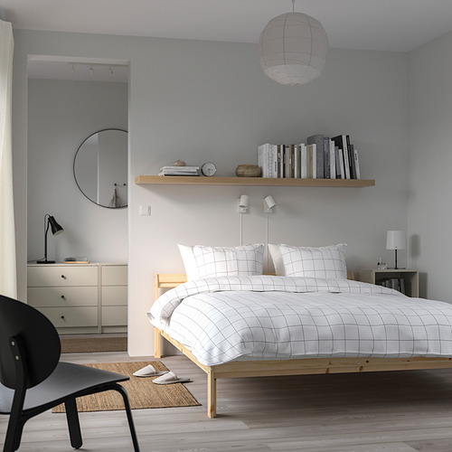 Dormitorio minimalista con cama NEIDEN, ropa de cama blanca, lámparas negras, paredes grises, suelo de madera, lámpara colgante y estantería.