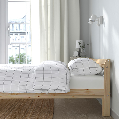 Dormitorio con cama de madera NEIDEN, ropa de cama de rejilla blanca, lámpara de noche y vista a la ciudad desde una gran ventana.