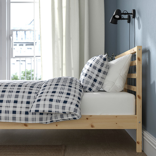 Cama de madera junto a la ventana, edredón de cuadros azules, aplique.