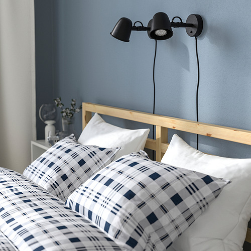 Dormitorio con paredes azules, un marco de cama de madera con un edredón a cuadros y dos luces negras montadas en la pared sobre la cama.