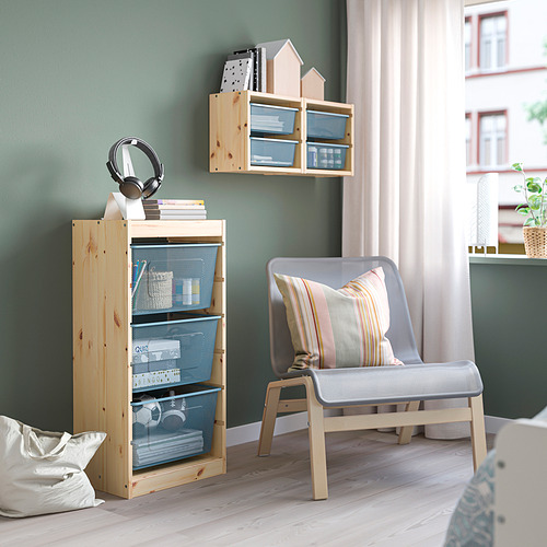 Almacenaje TROFAST en madera clara y azul con cajones de malla y mueble alto para libros. Silla gris con almohada en habitación verde.