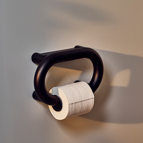 Porta papel higiénico negro con diseño redondeado, montado sobre pared gris. Sostiene un rollo de papel higiénico blanco.
