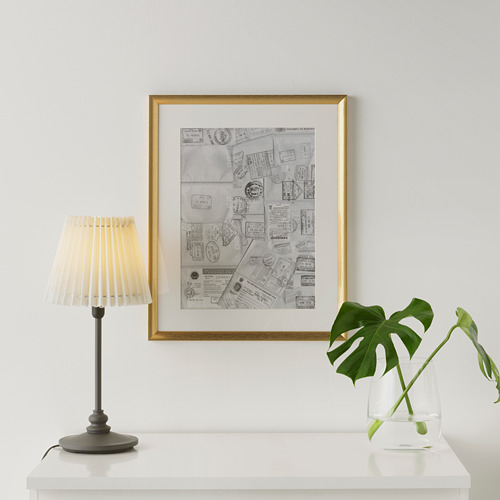 Arte de collage enmarcado sobre un estante blanco, iluminado por una lámpara, al lado de la planta.