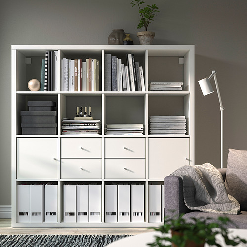 Estantería KALLAX de Ikea con libros, cajones y archivos. Al lado de una silla y una lámpara.