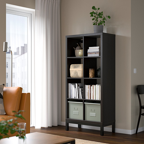 Estantería negra KALLAX con cubos verdes, más alta que una silla, diseño aireado.