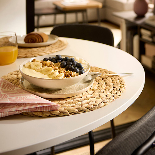 Mesa de comedor con yogur, granola, frutas en un mantel individual tejido.