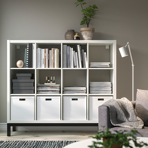 La estantería blanca KALLAX contiene libros y decoración. Su gran tamaño se adapta a muchos artículos, exhibidos de manera prominente contra una pared.