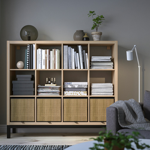 Estantería KALLAX con libros, decoración, plantas y cajas de almacenaje, sillón gris parcial.